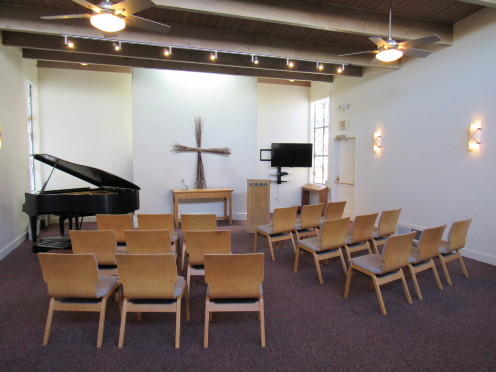 small chapel with altar, chairs piano, TV screen, podium, cross