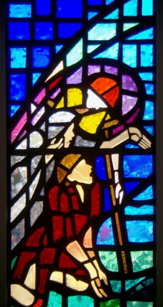 Stained glass window of 3 figures reaching out representative of the Gospel stories of Ministry to the poor, lame and blind