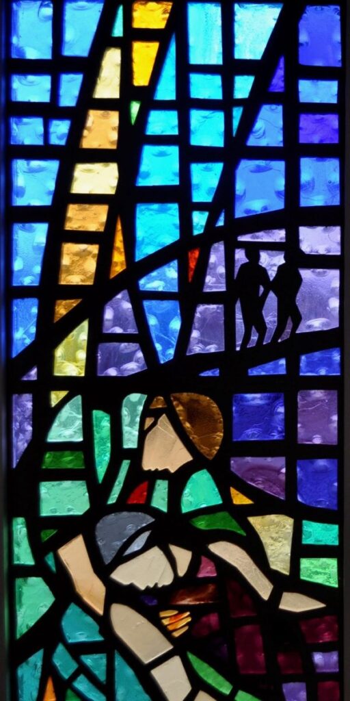 Stained glass window of a man caring for another man representative of the Luke story of the Good Samaritain