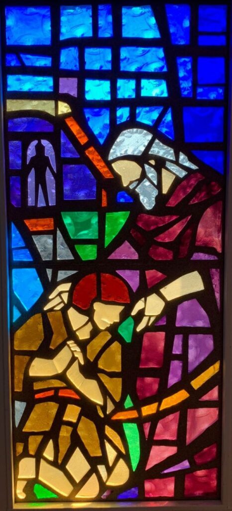 Stained glass window of a man on his knees in front of an older man representative of the Luke story of the Prodigal Son