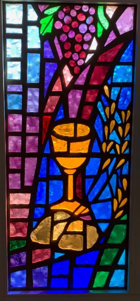 Stained glass window of grapes hanging over a chalice representative of the Matthew, Mark and 1 Corinthians stories of the Lord's Supper