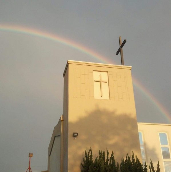 A real rainbow goes over the steeple of the church with two crosses shown.